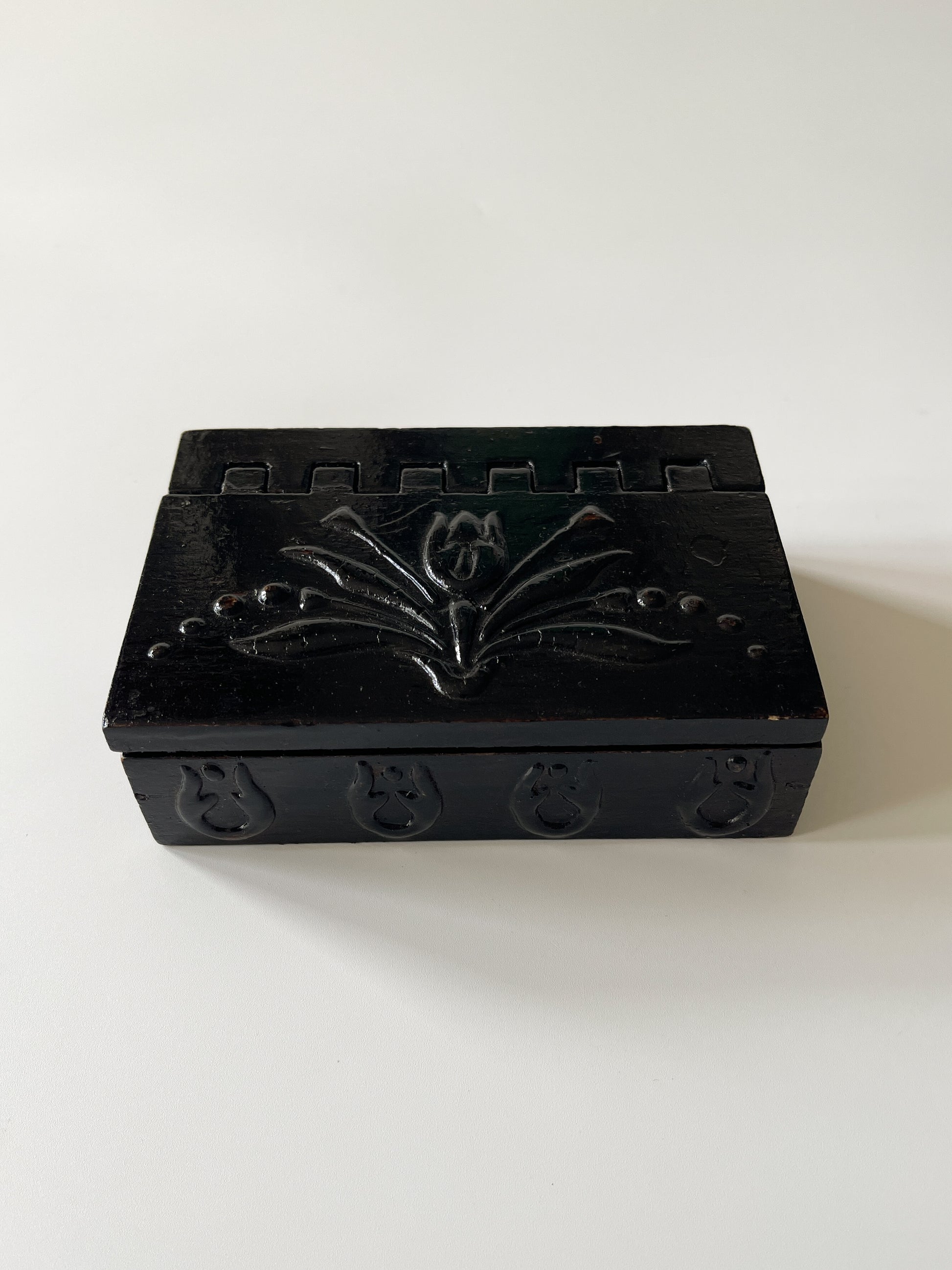 Black decorative box with intricate carvings on a white background